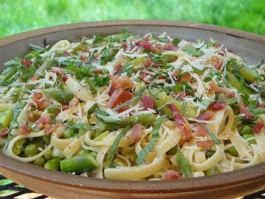 a bowl of fettuccine pasta with asparagus, bacon, peas, and cheese 