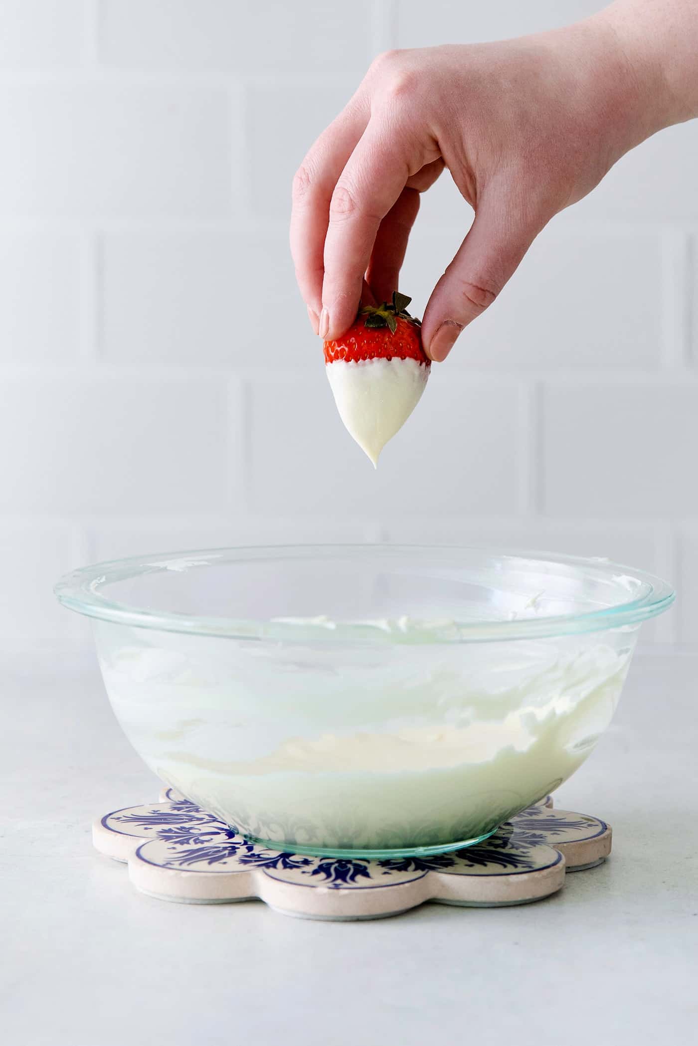 A hand holding a strawberry dipped in white chocolate