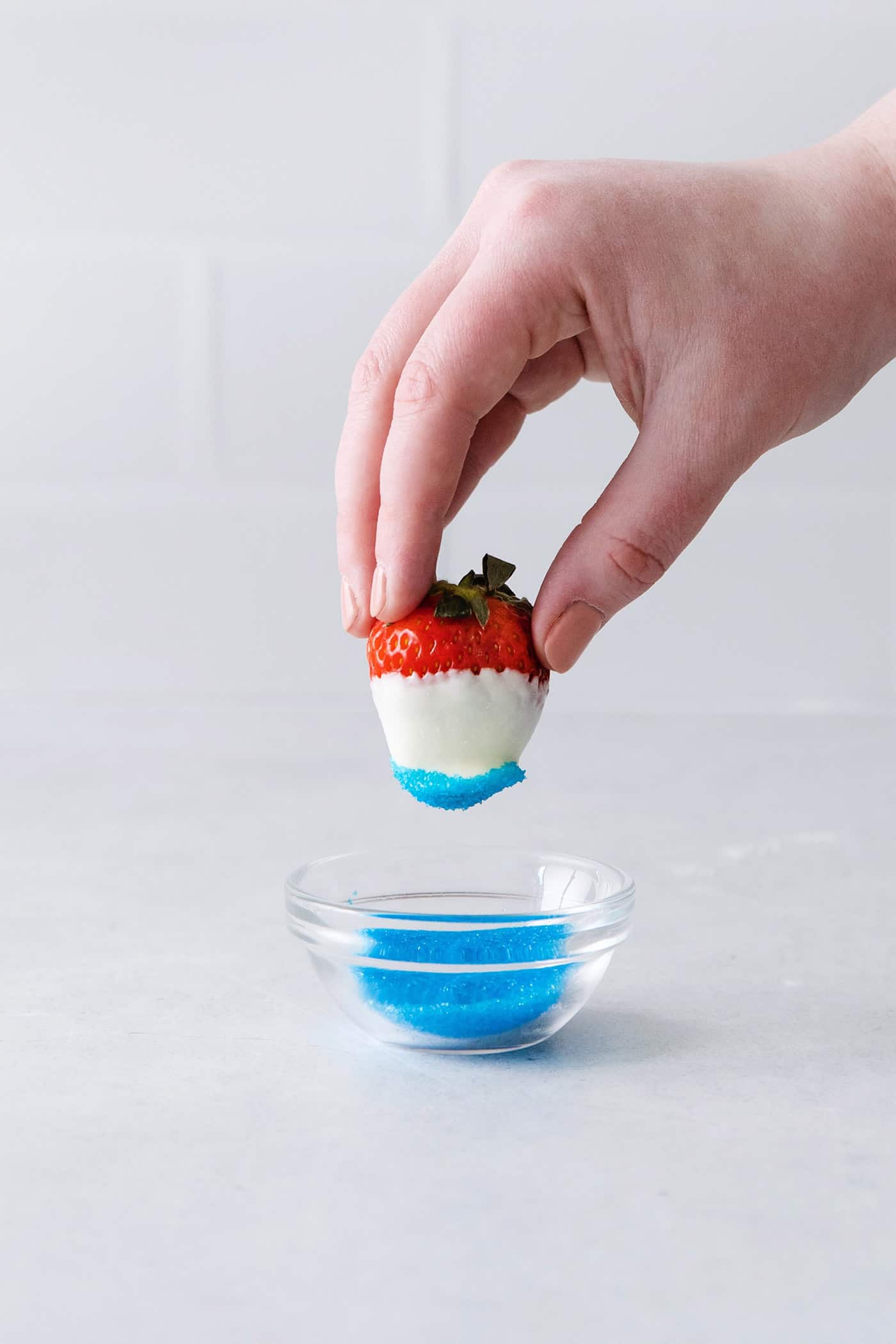 A hand holding a strawberry dipped in blue sugar