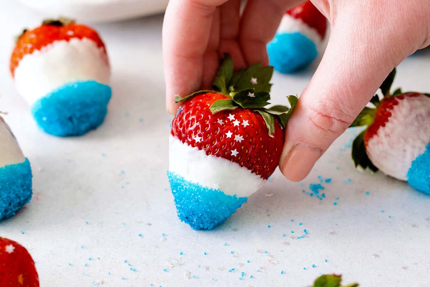 A hand holding a white chocolate covered strawberry dipped in blue sugar