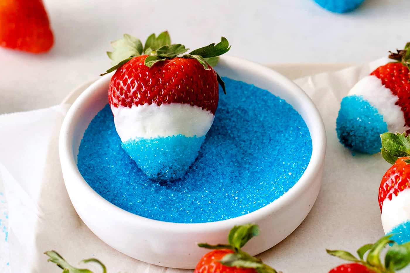 A white chocolate dipped strawberry in a bowl of blue sugar