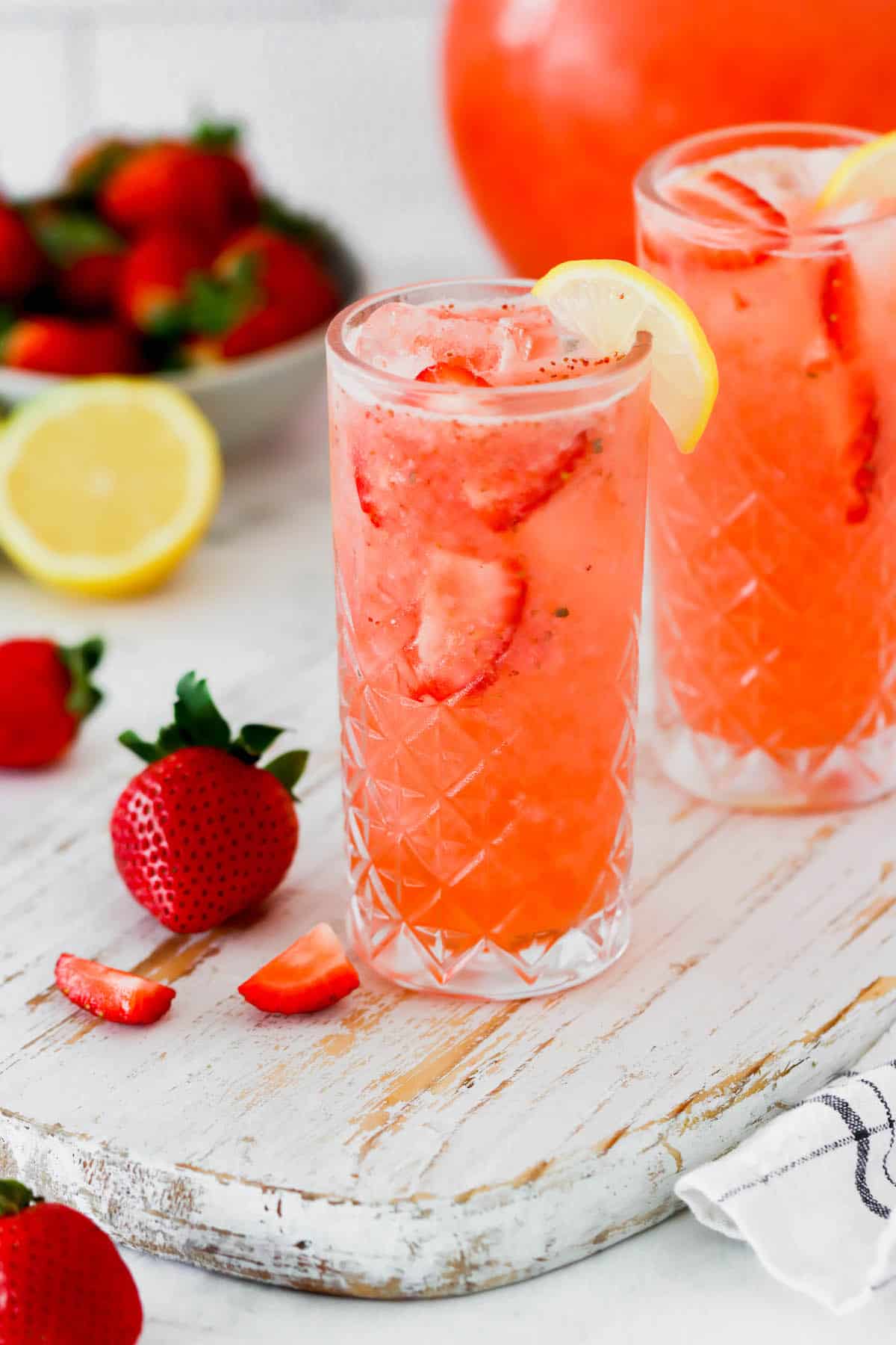 A glass of strawberry lemonade garnished with strawberry slices and a lemon wedge