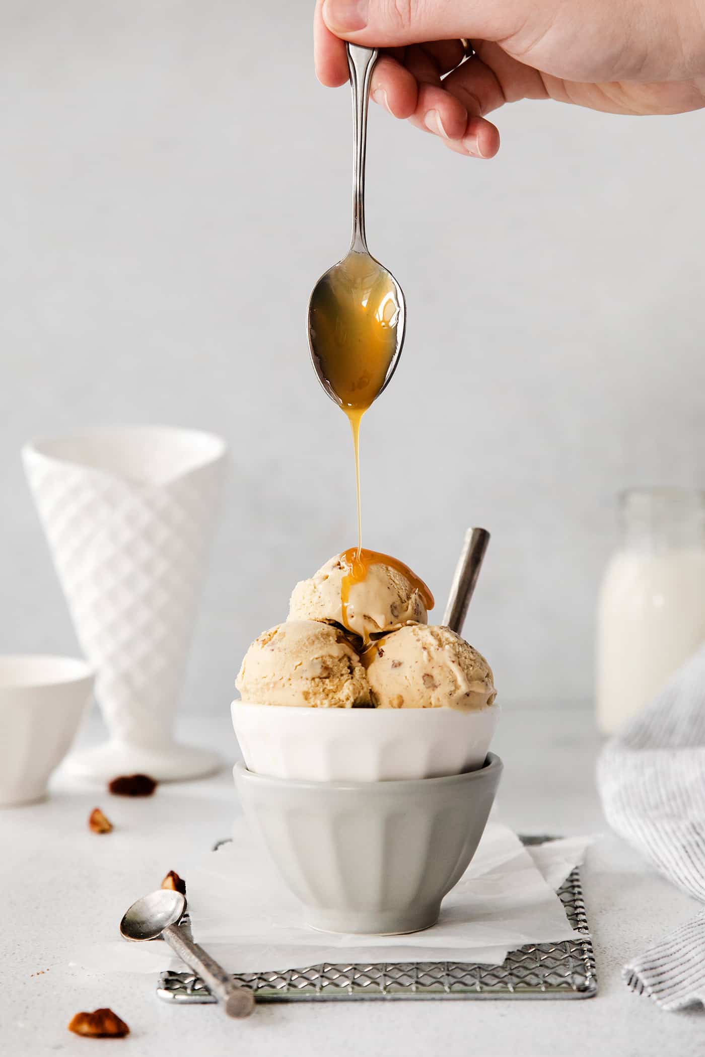 A spoon drizzling caramel over butter pecan ice cream