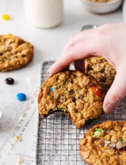 A hand holding a monster cookie with a bite missing