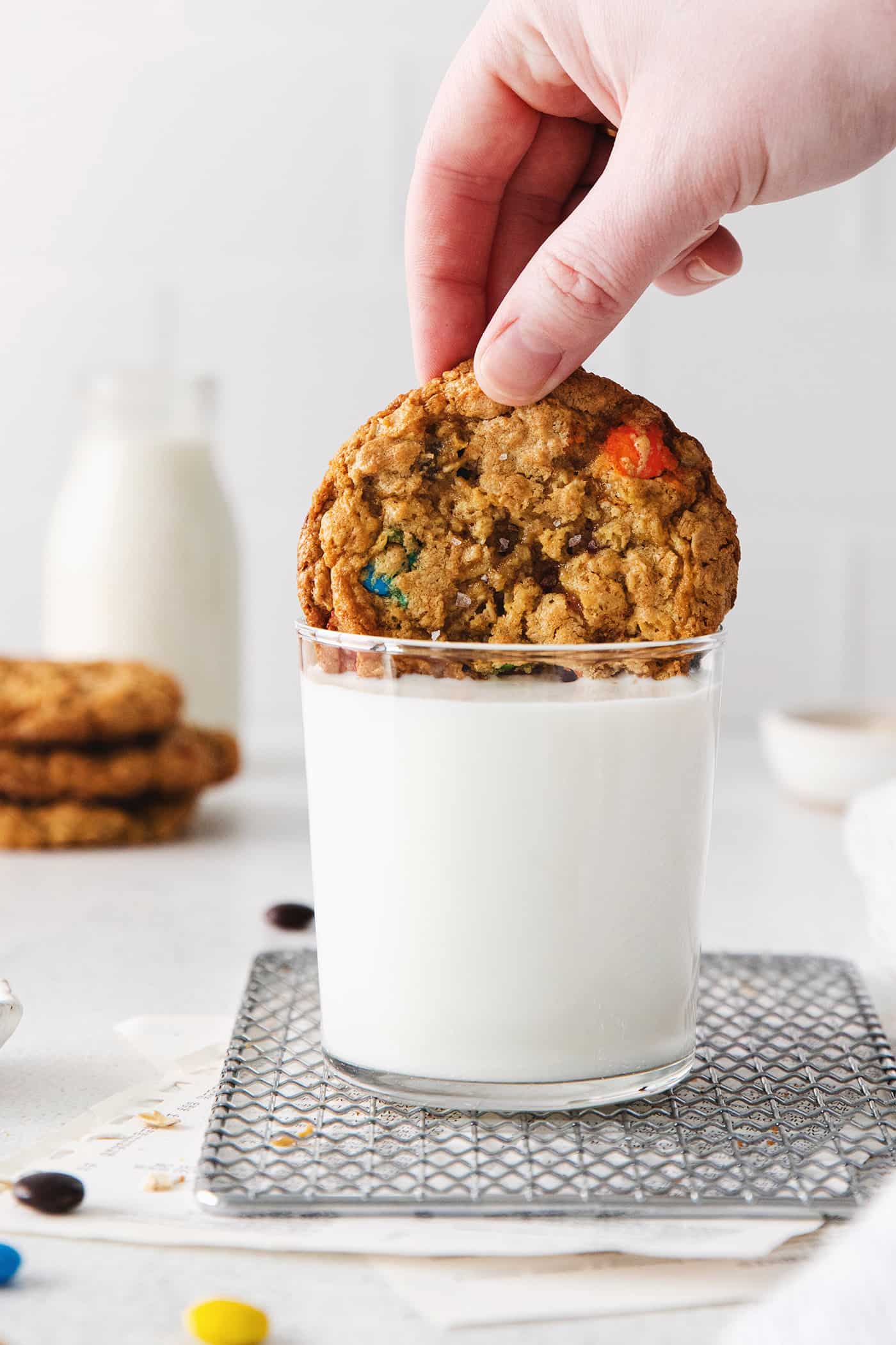 A hand dipping a monster cookie into a glass of milk