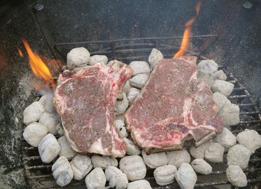 two steaks being grilled directly on charcoal