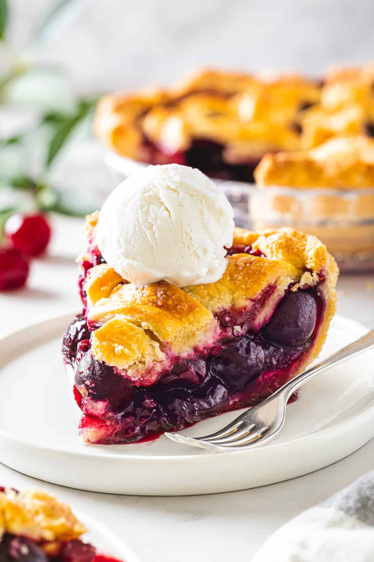 A slice of cherry pie topped with a scoop of ice cream
