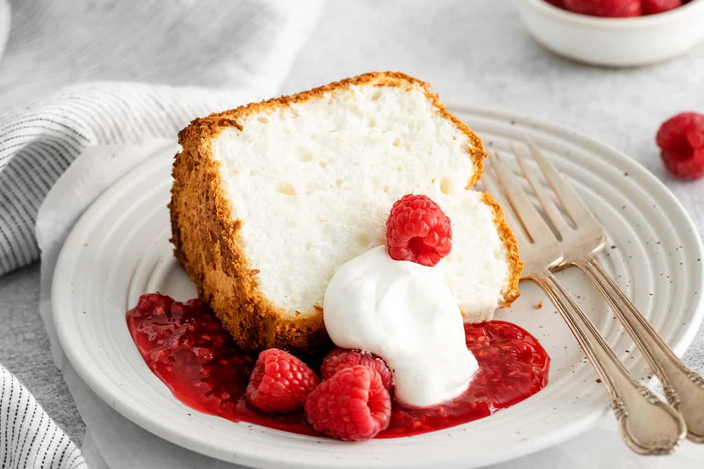 A slice of angel food cake with raspberry sauce and whipped cream
