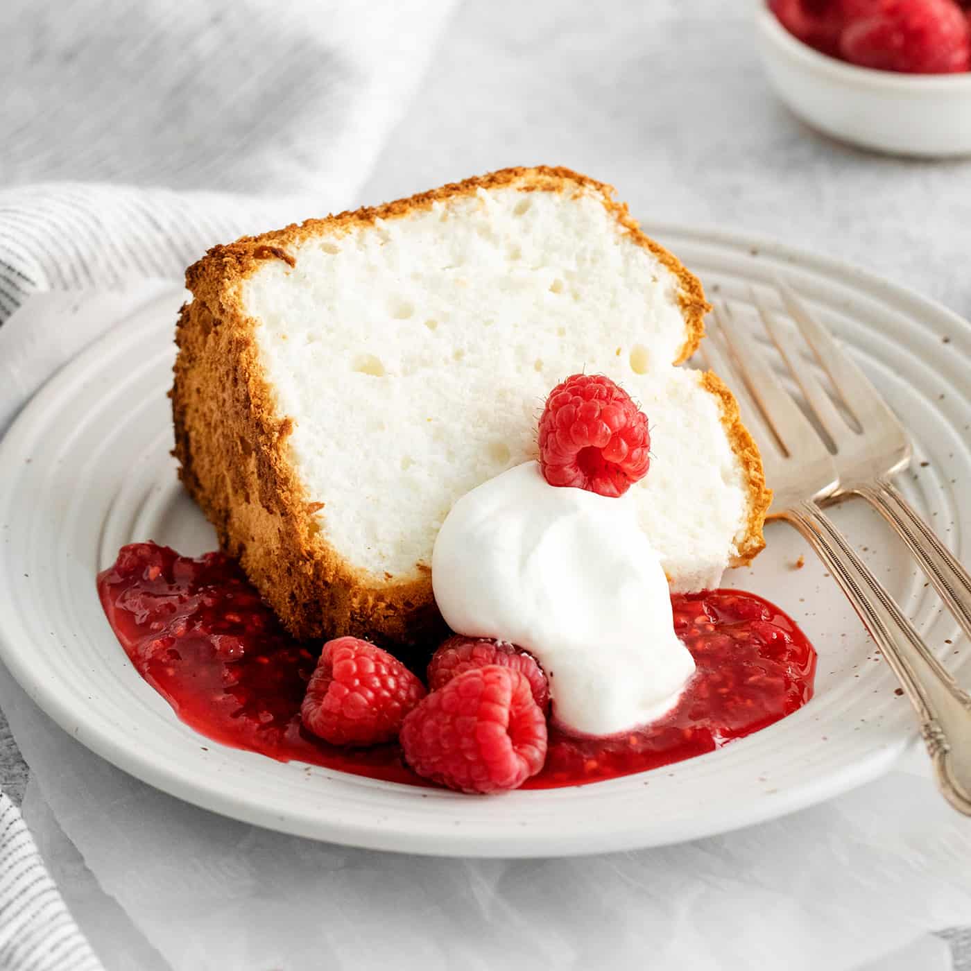 A slice of angel food cake with raspberry sauce and whipped cream