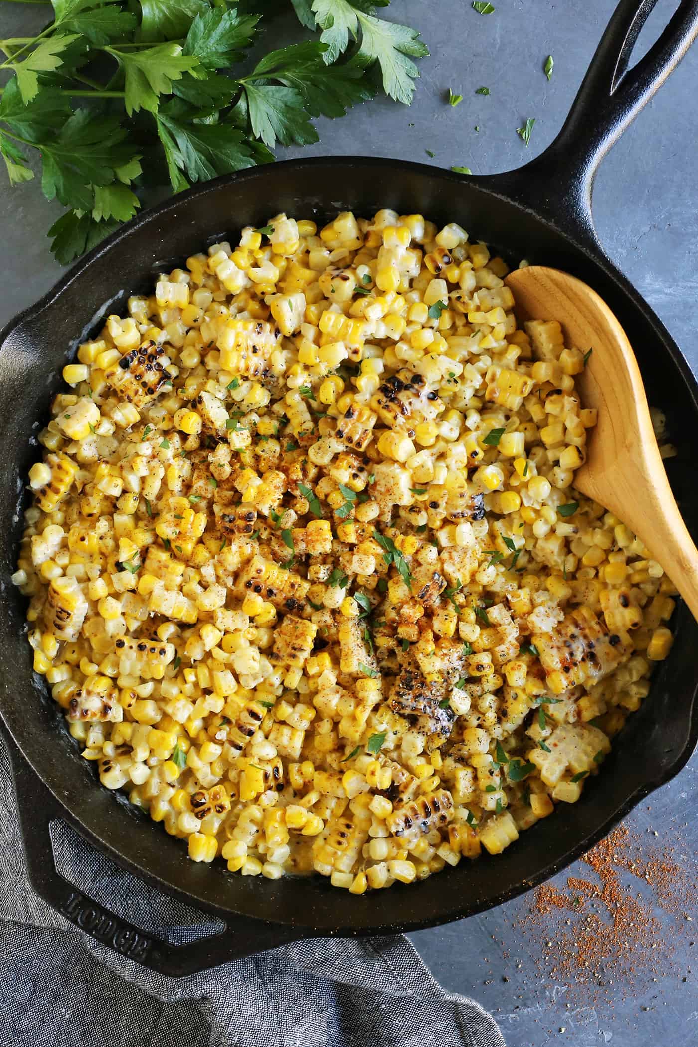 A wooden spoon stirring grilled creamed corn in a cast iron skillet