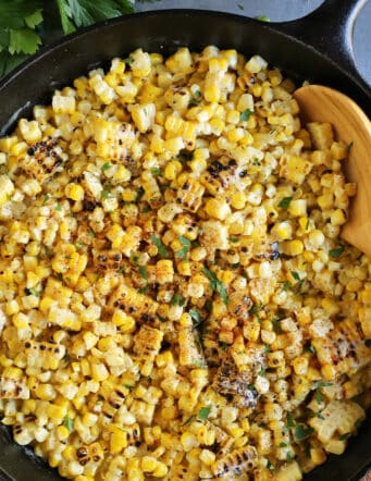 Close-up of a spoon stirring grilled creamed corn in a cast iron skillet