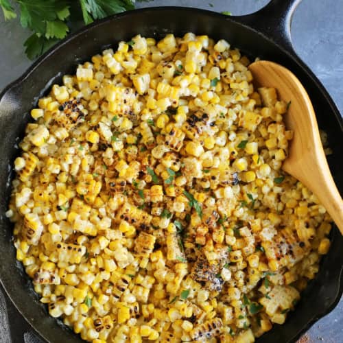 Close-up of a spoon stirring grilled creamed corn in a cast iron skillet