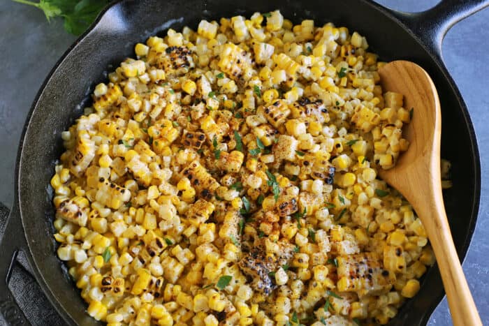 A wooden spoon stirring grilled creamed corn