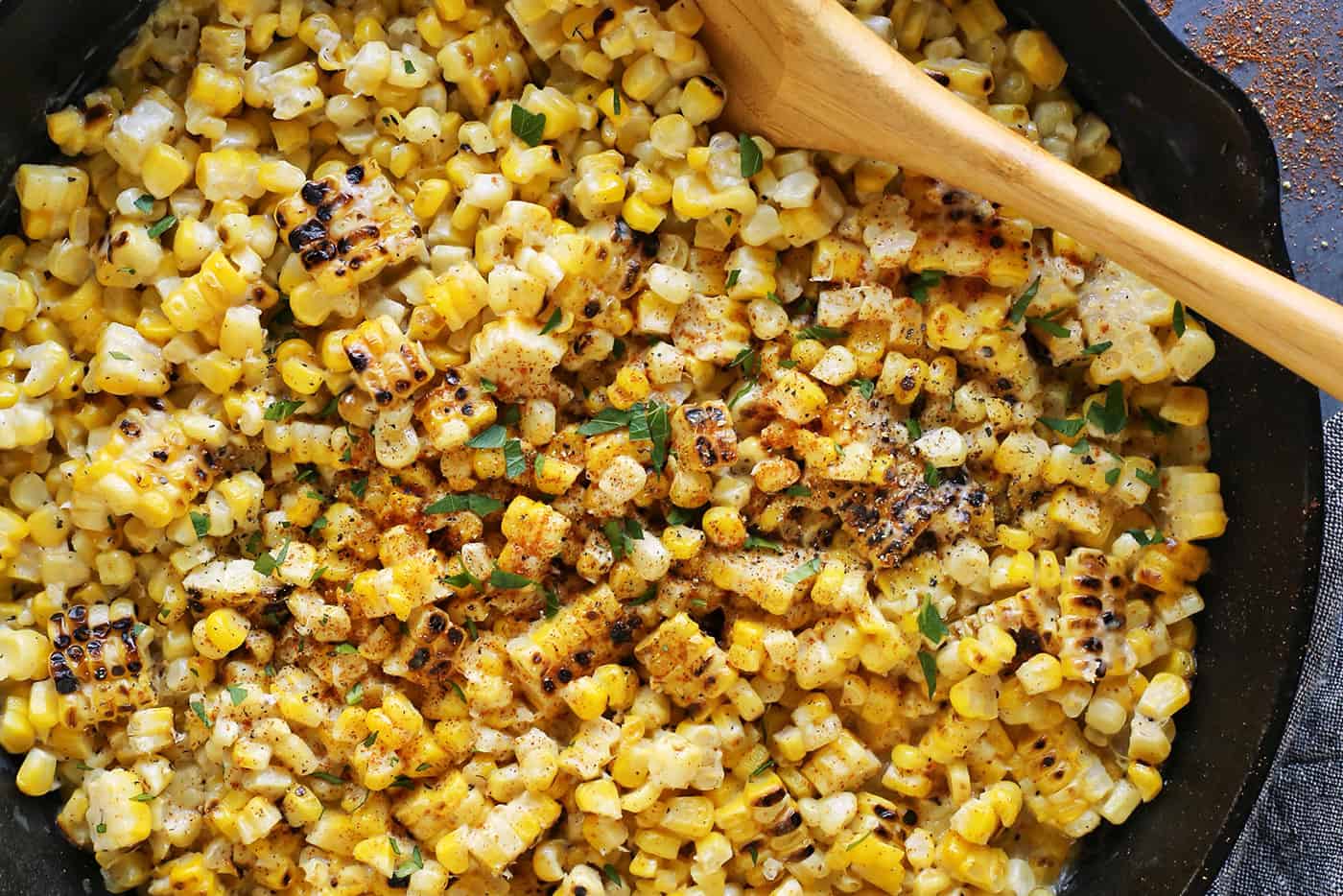 Close-up of grilled creamed corn in a skillet with a wooden spoon