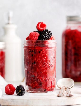 Front view of a jar of freezer jam topped with raspberries and blackberries