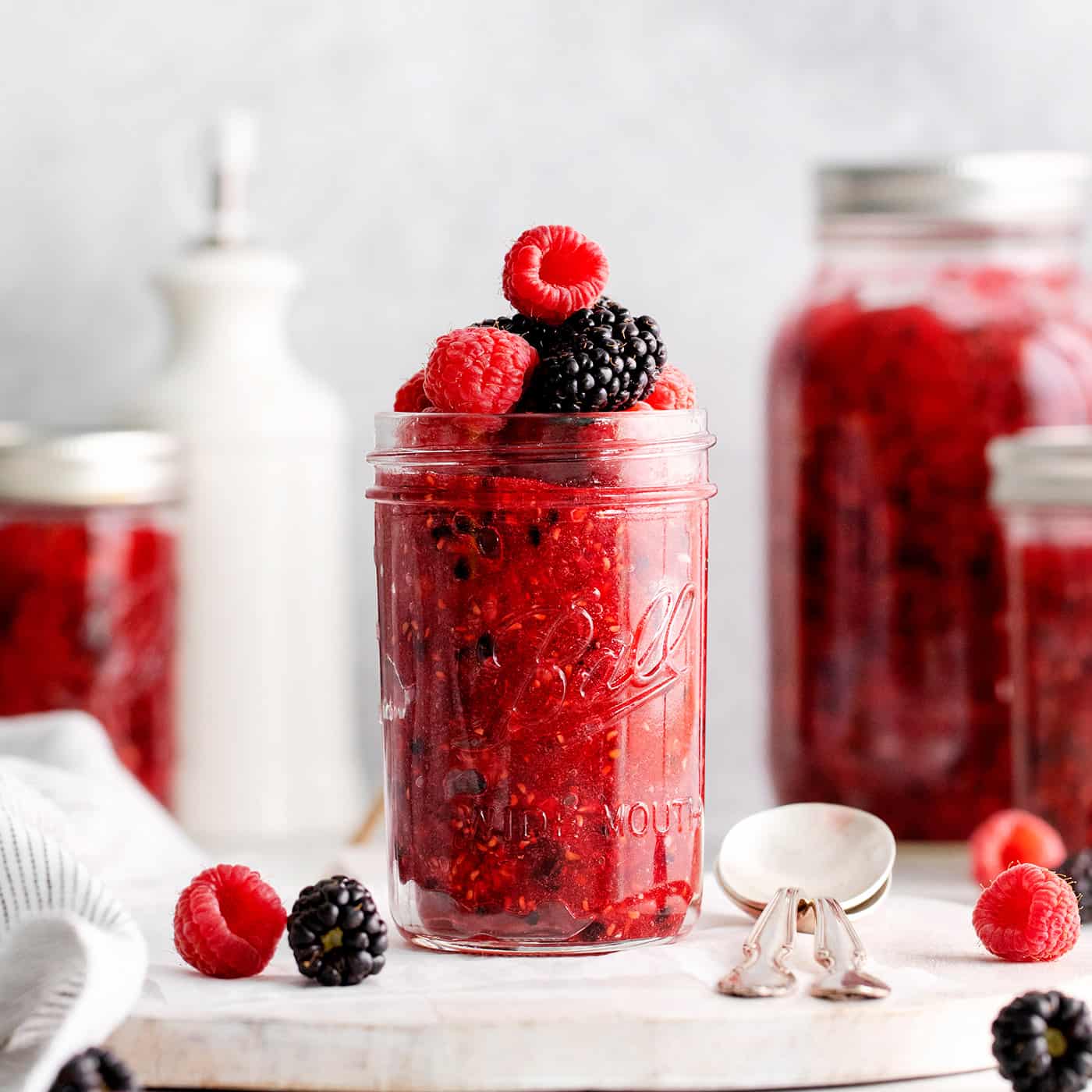 Front view of a jar of freezer jam topped with raspberries and blackberries