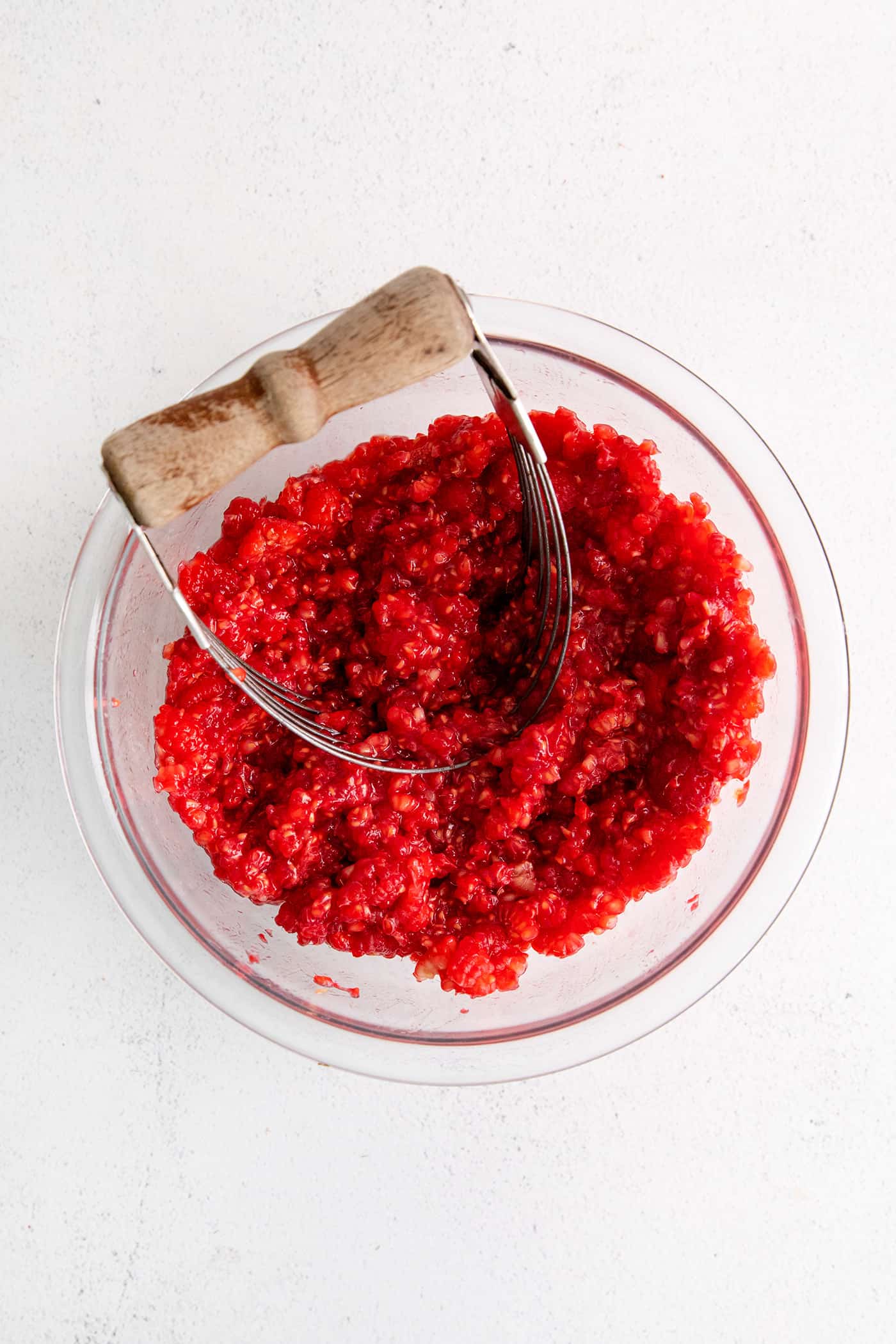 A potato masher mashing raspberries