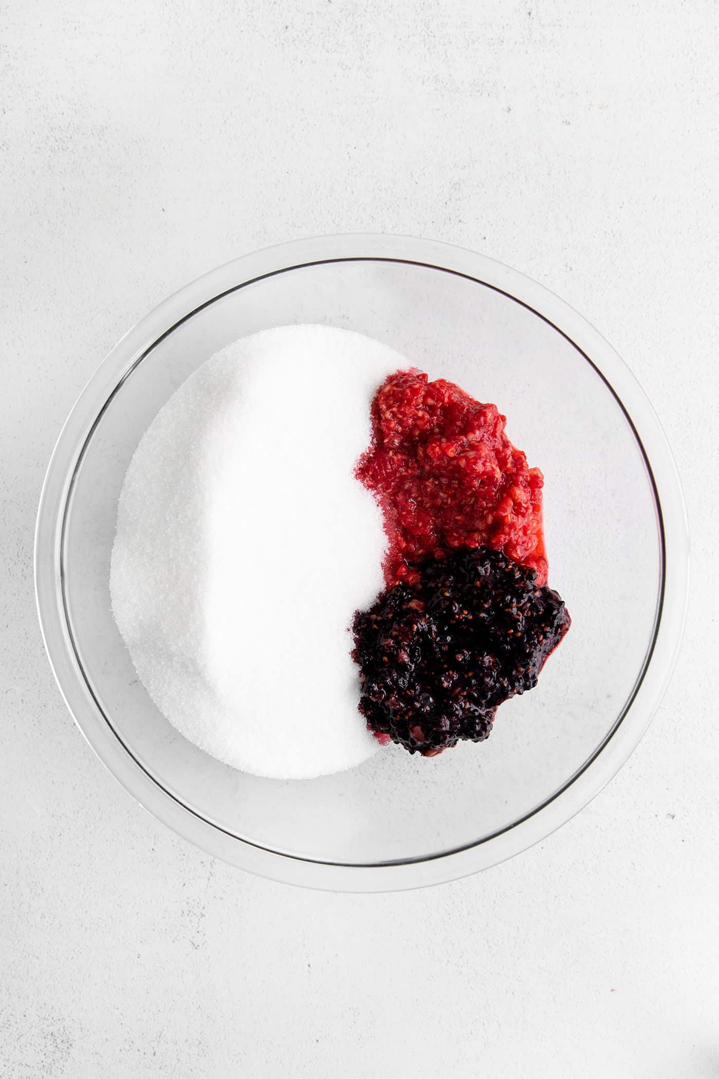 Mashed raspberries and blackberries in a bowl with sugar