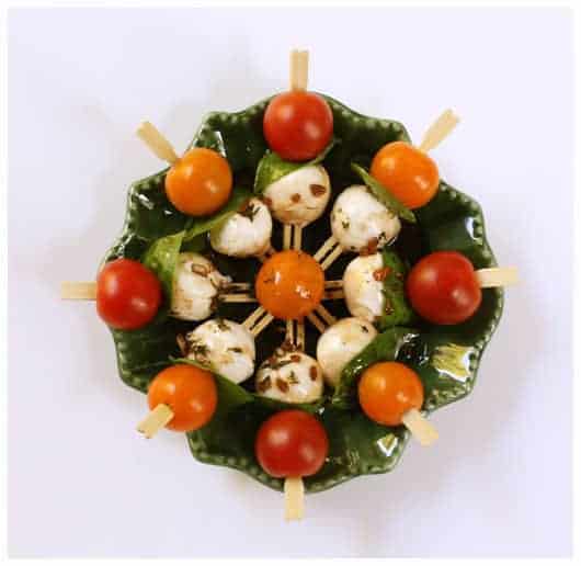 Mini kabobs with cherry tomato, basil, and mozzarella balls arranged in a round dish