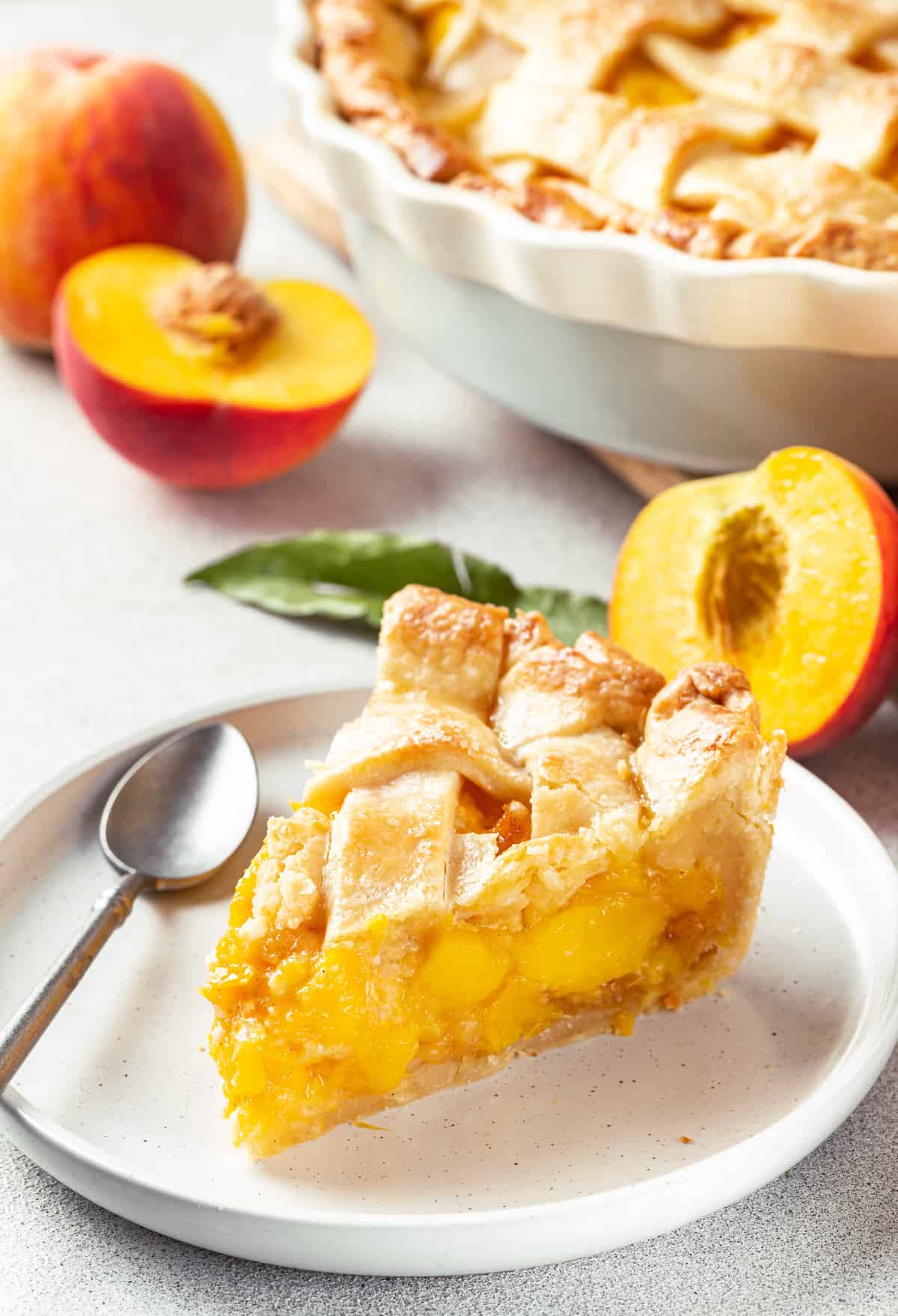 Made with just 10 ingredients, this Homemade Peach Pie is perfectly spiced and topped with a beautiful golden brown flaky lattice crust. A slice of peach pie on a white plate