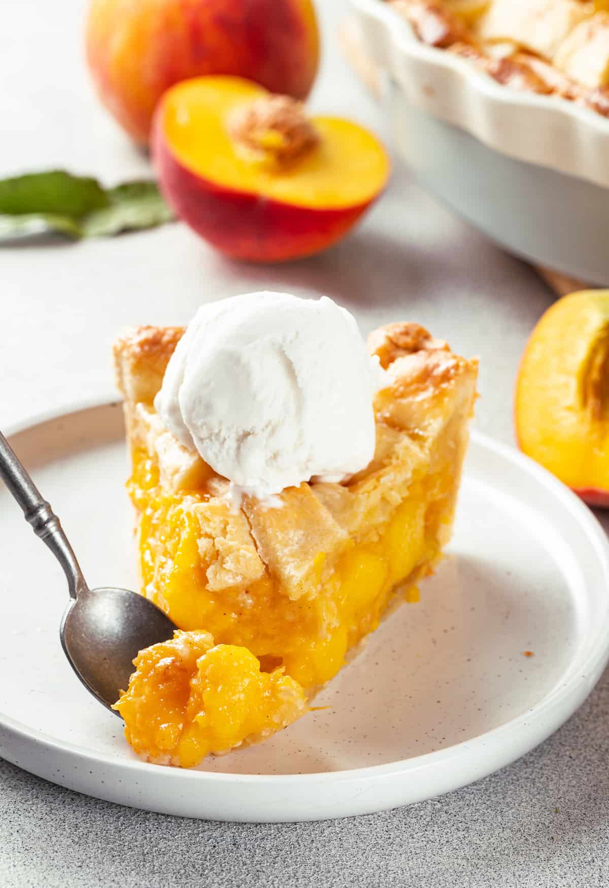 A slice of peach pie topped with a scoop of ice cream