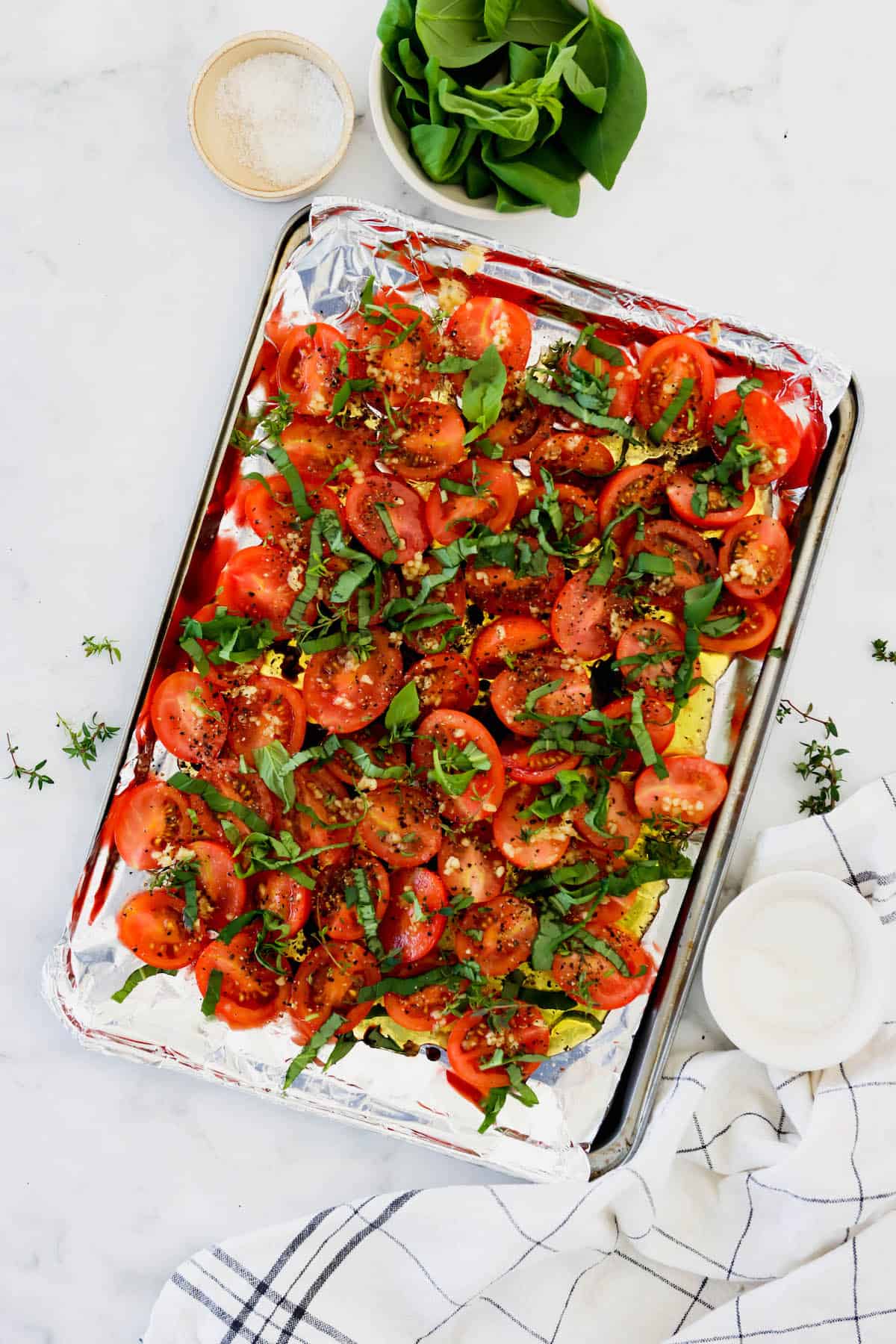 overhead view of roasted tomatoes with basil and thyme on a sheet pan