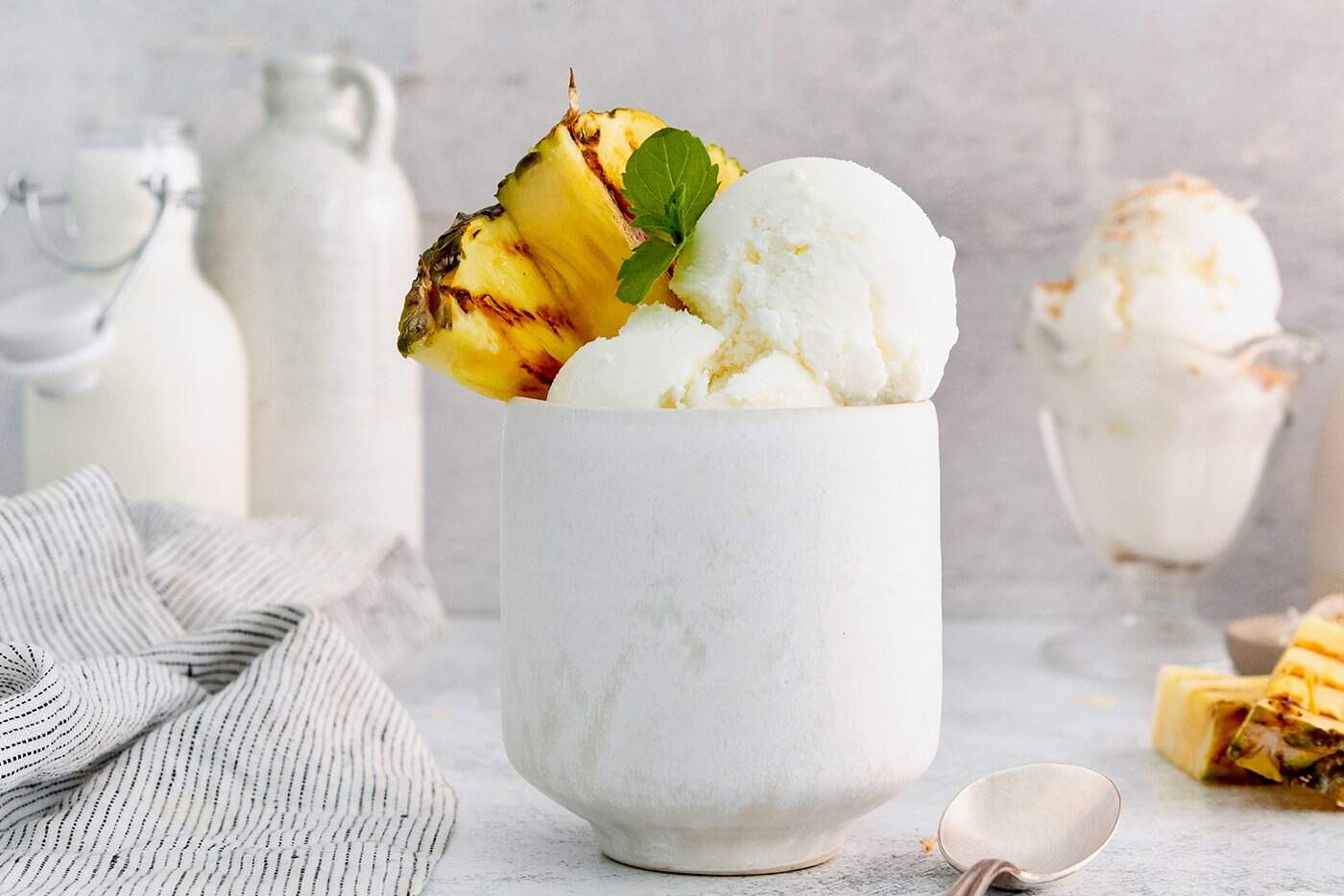 Coconut ice cream in tall bowl with grilled pineapple and sprig of mint
