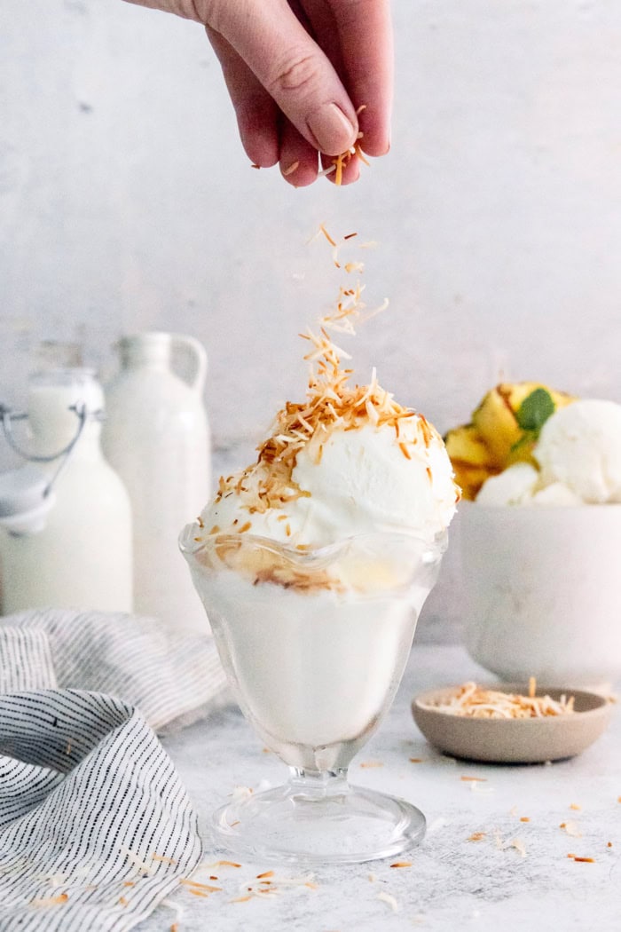 Hand sprinkling toasted coconut onto coconut ice cream in glass dish