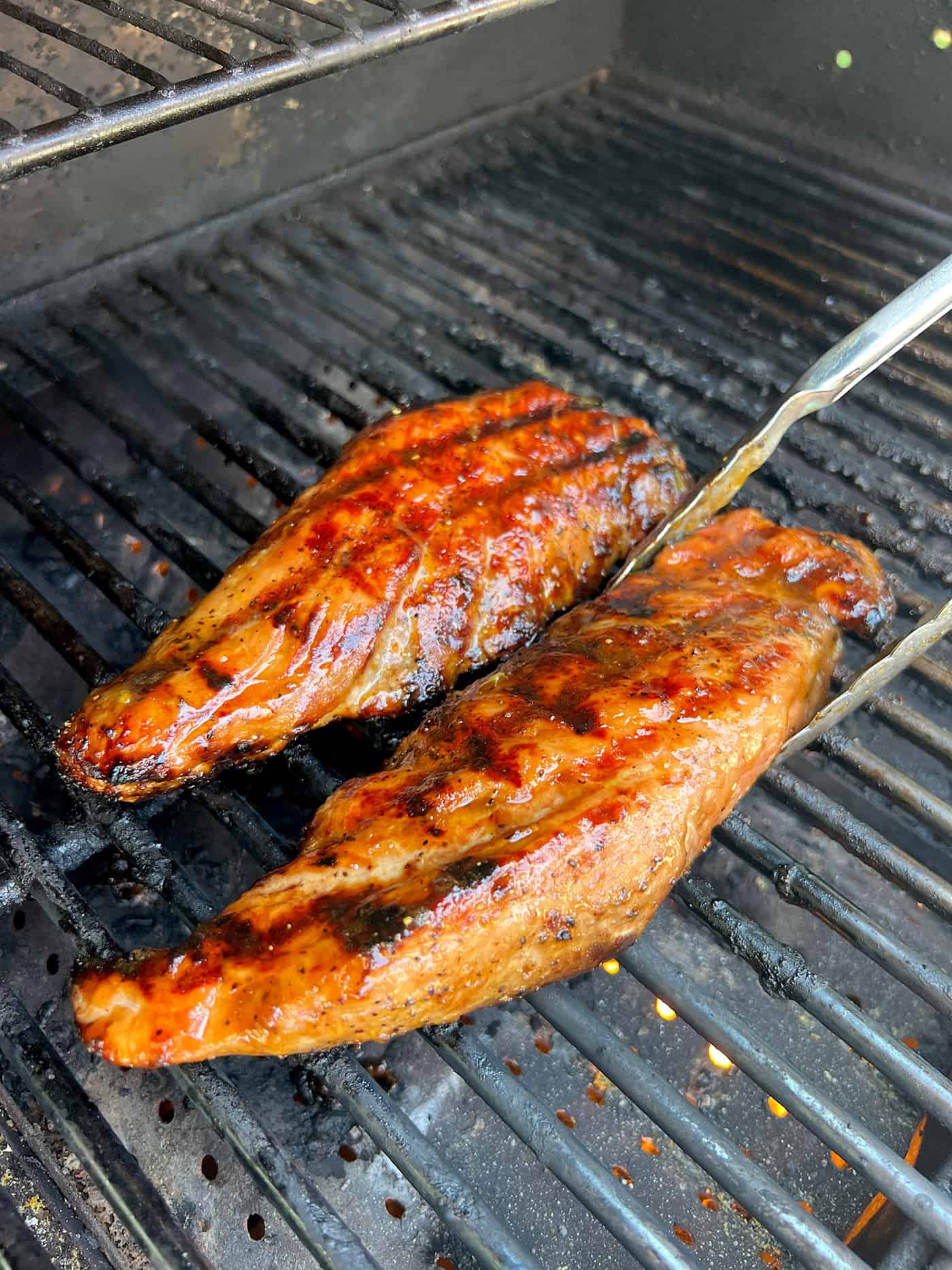 Tongs removing a pork tenderloin from the grill