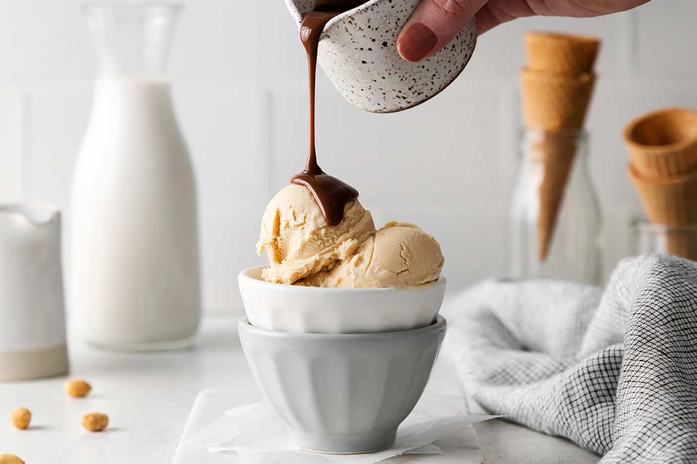 A hand pouring hot fudge sauce over peanut butter ice cream