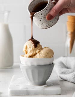 A hand pouring hot fudge sauce over peanut butter ice cream