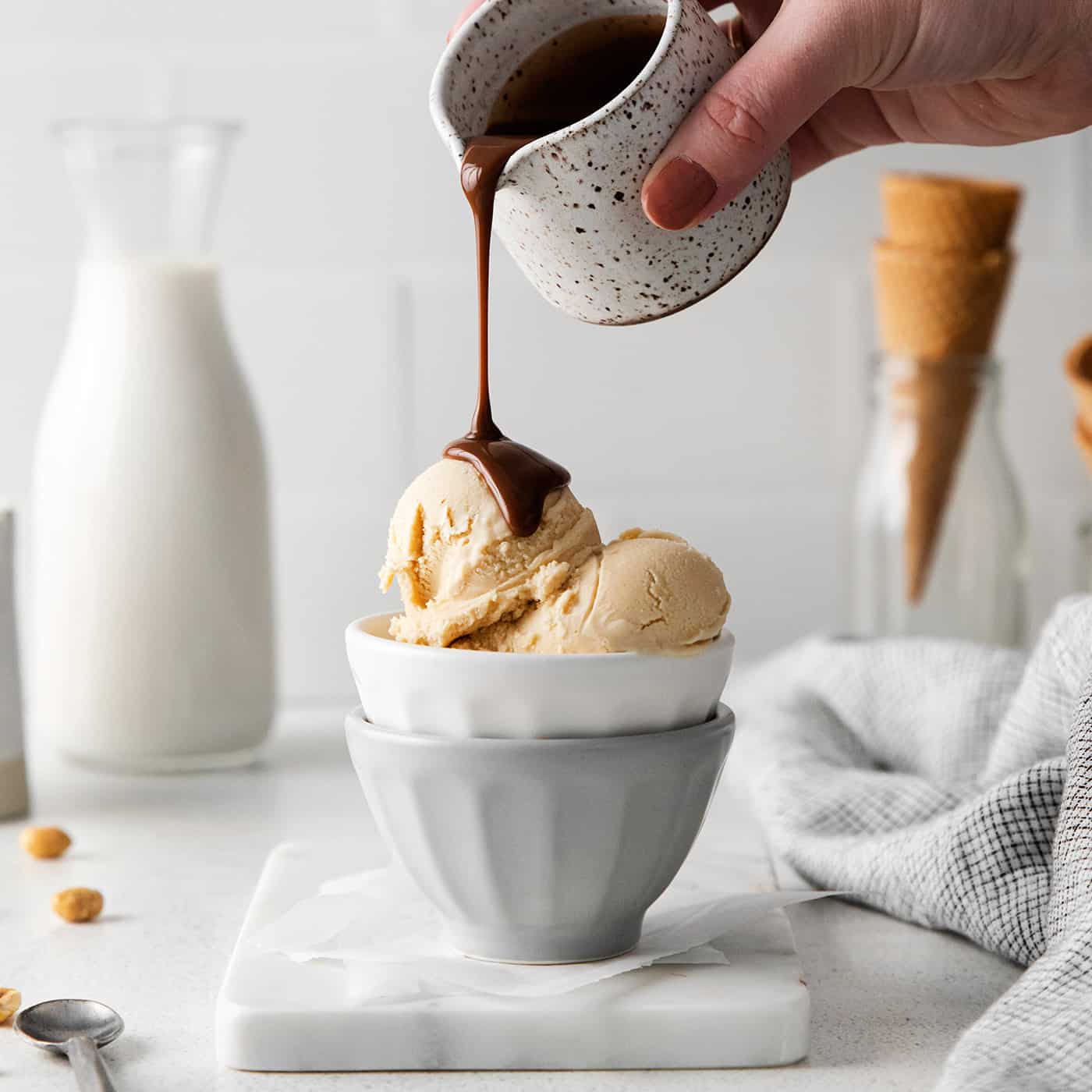 A hand pouring hot fudge sauce over peanut butter ice cream