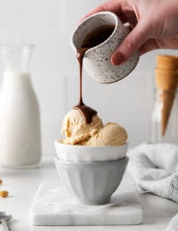 A hand pouring hot fudge sauce over peanut butter ice cream