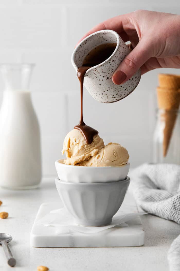 A hand pouring hot fudge sauce over peanut butter ice cream