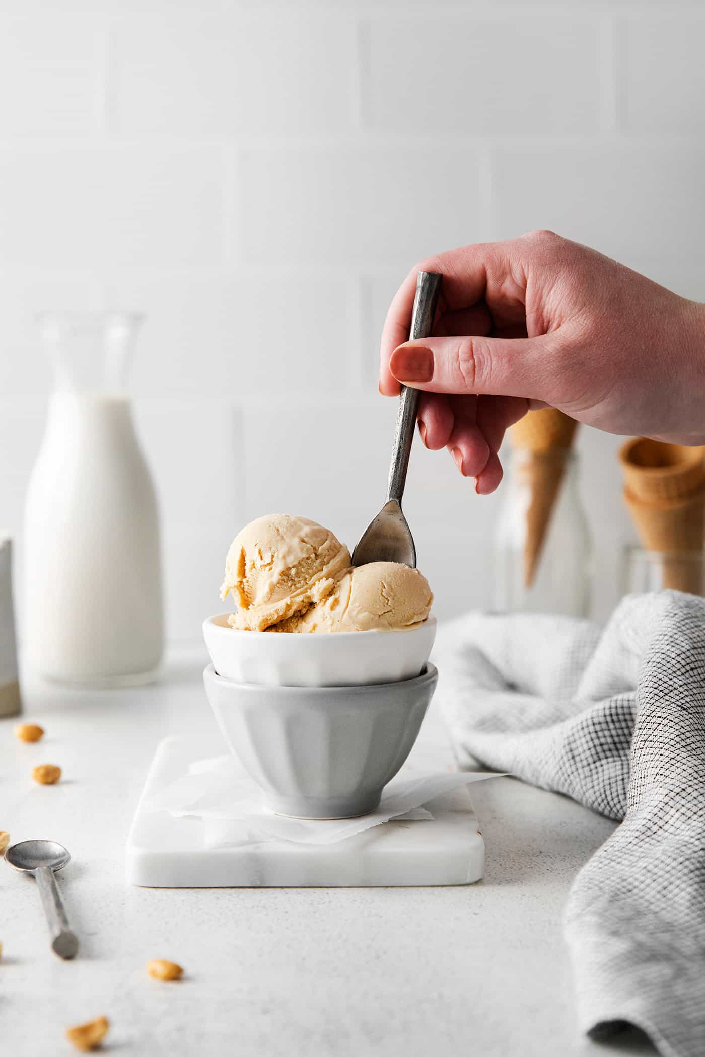 A hand holding a spoon in a bowl of peanut butter ice cream