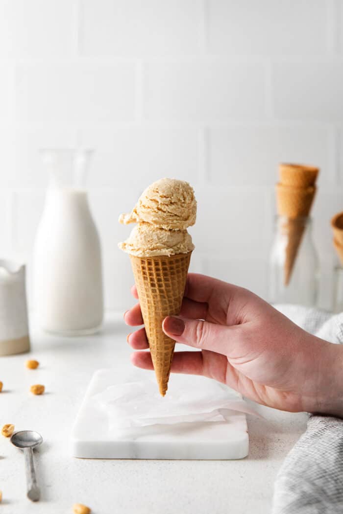 A hand holding a waffle cone with scoops of homemade peanut butter ice cream