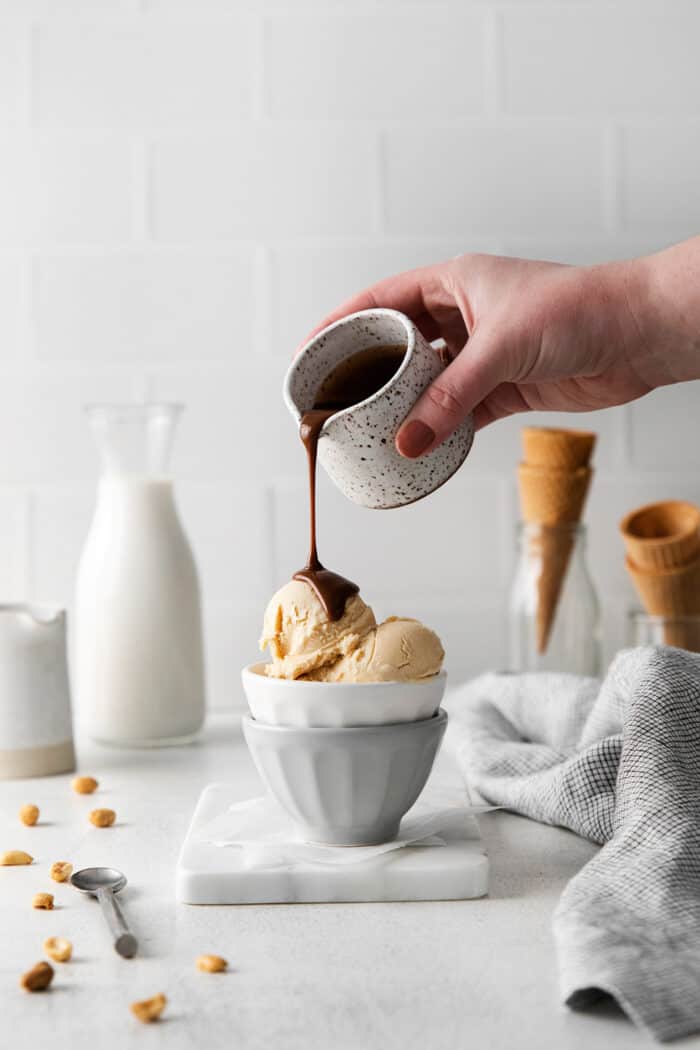 A hand pouring hot fudge sauce over peanut butter ice cream