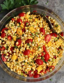 Sweet corn salad in a glass bowl with a spoon stirring it