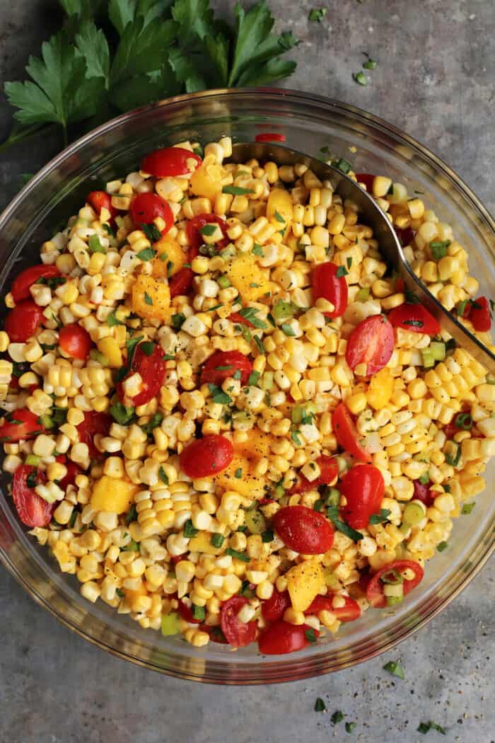 Sweet corn salad in a glass bowl with a spoon stirring it