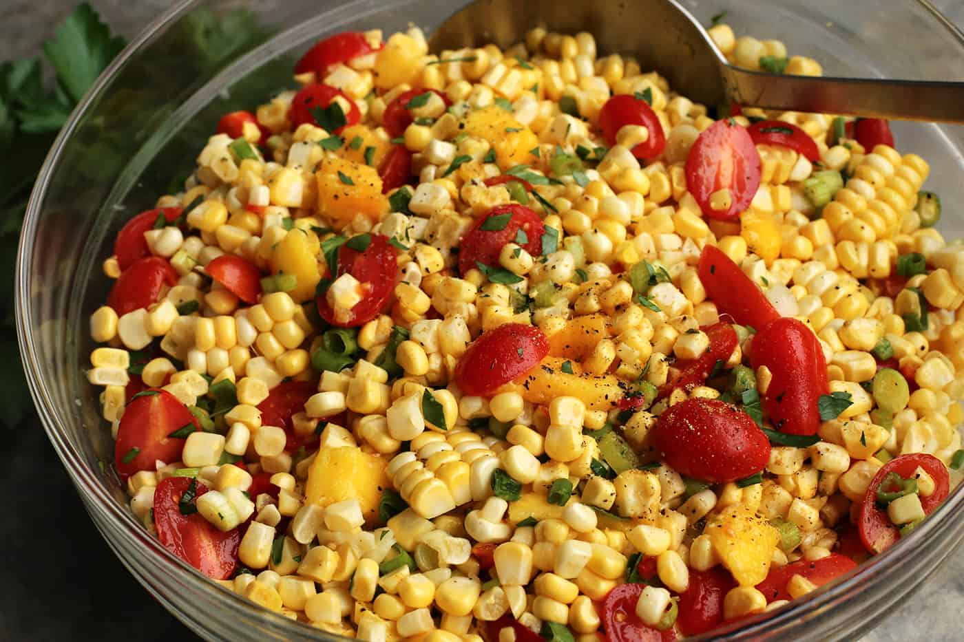 A spoon stirring tomato and sweet corn salad