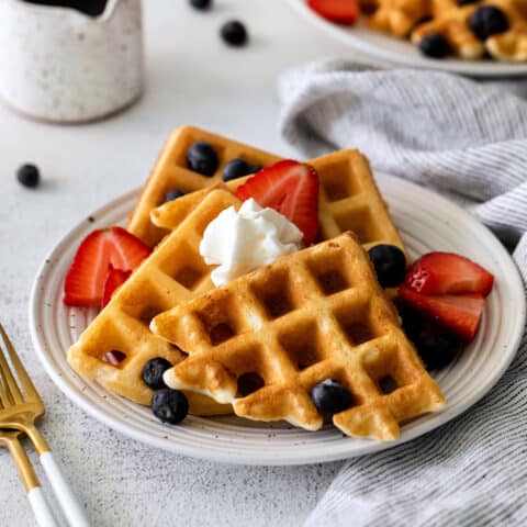 Yeast waffles on a plate with berries and whipped cream