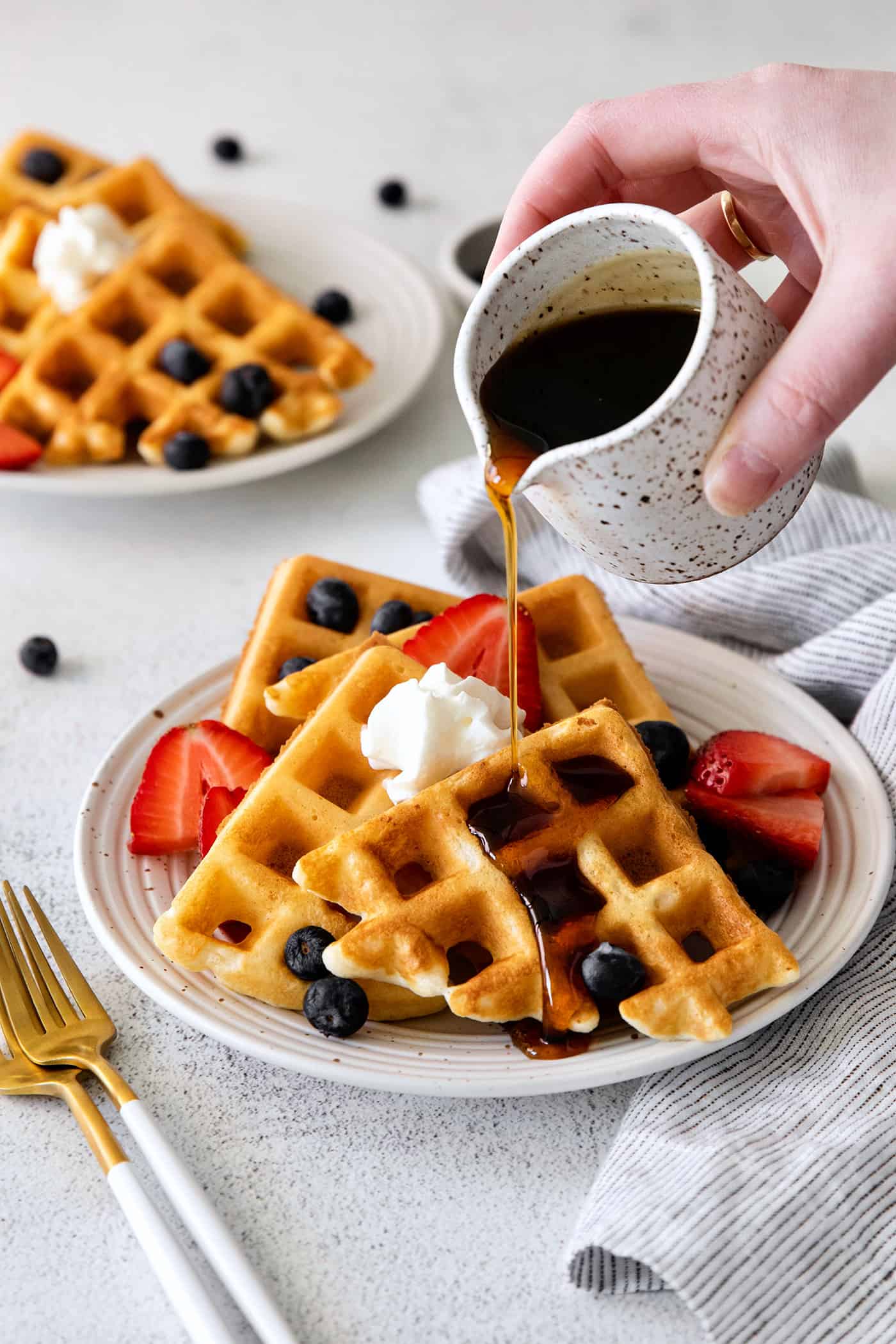 Syrup being poured over waffles on a plate