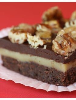 A three-layered brownie topped with chopped pecans and a layer of white chocolate caramel in the center.
