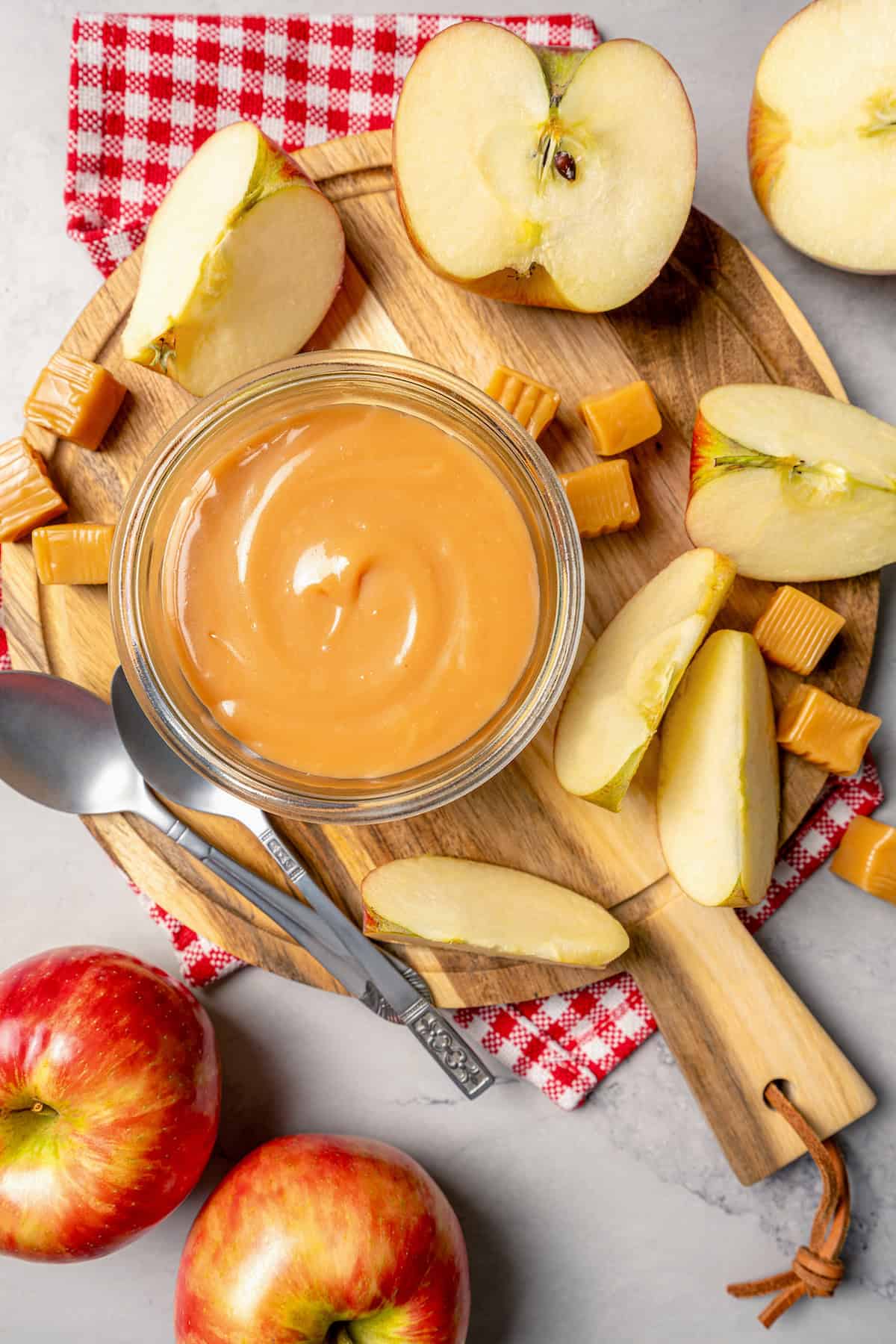 Overhead view of wooden board with jar of caramel apple dip and apple slices