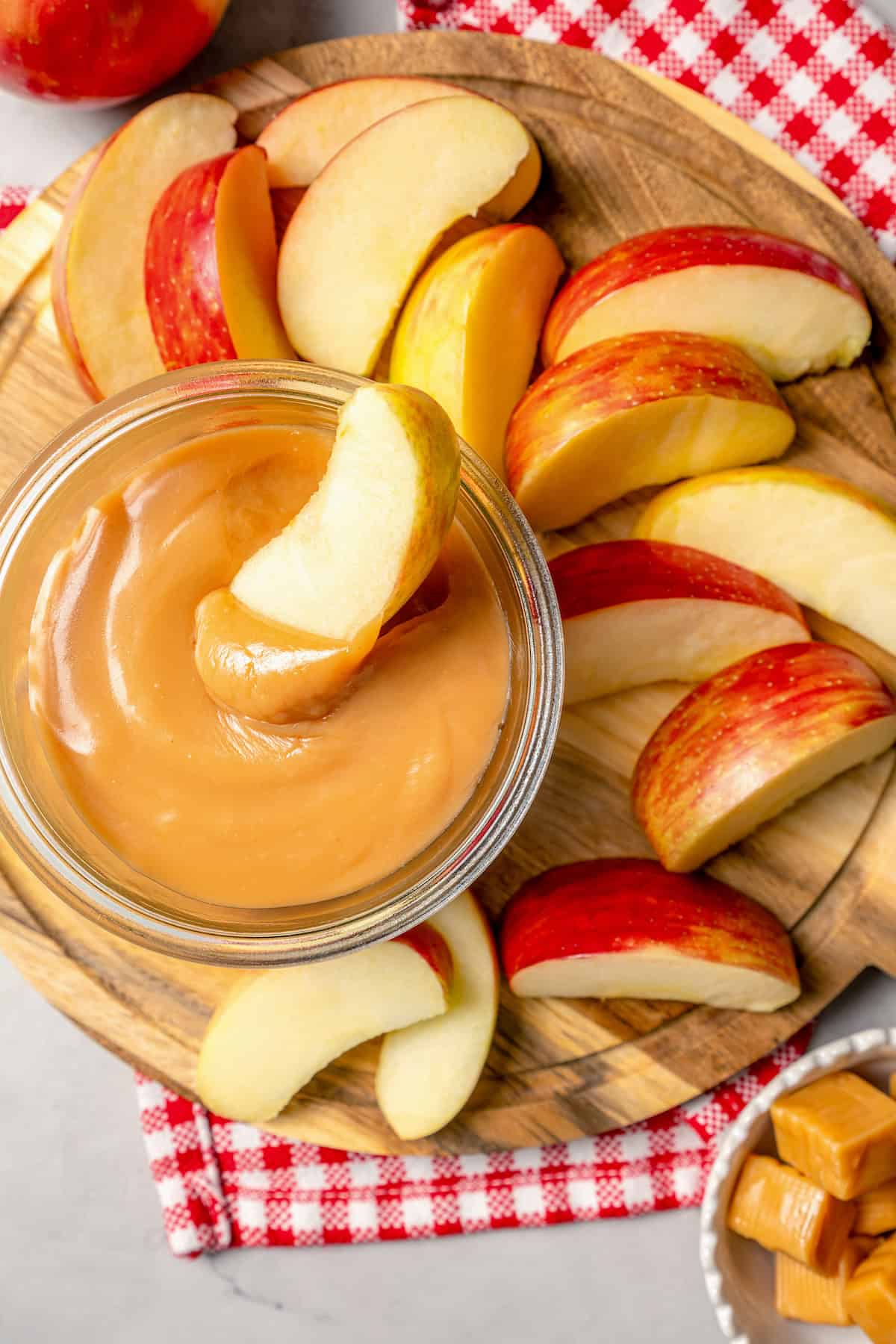 Overhead view of apple slices on wooden board with jar of caramel apple dip
