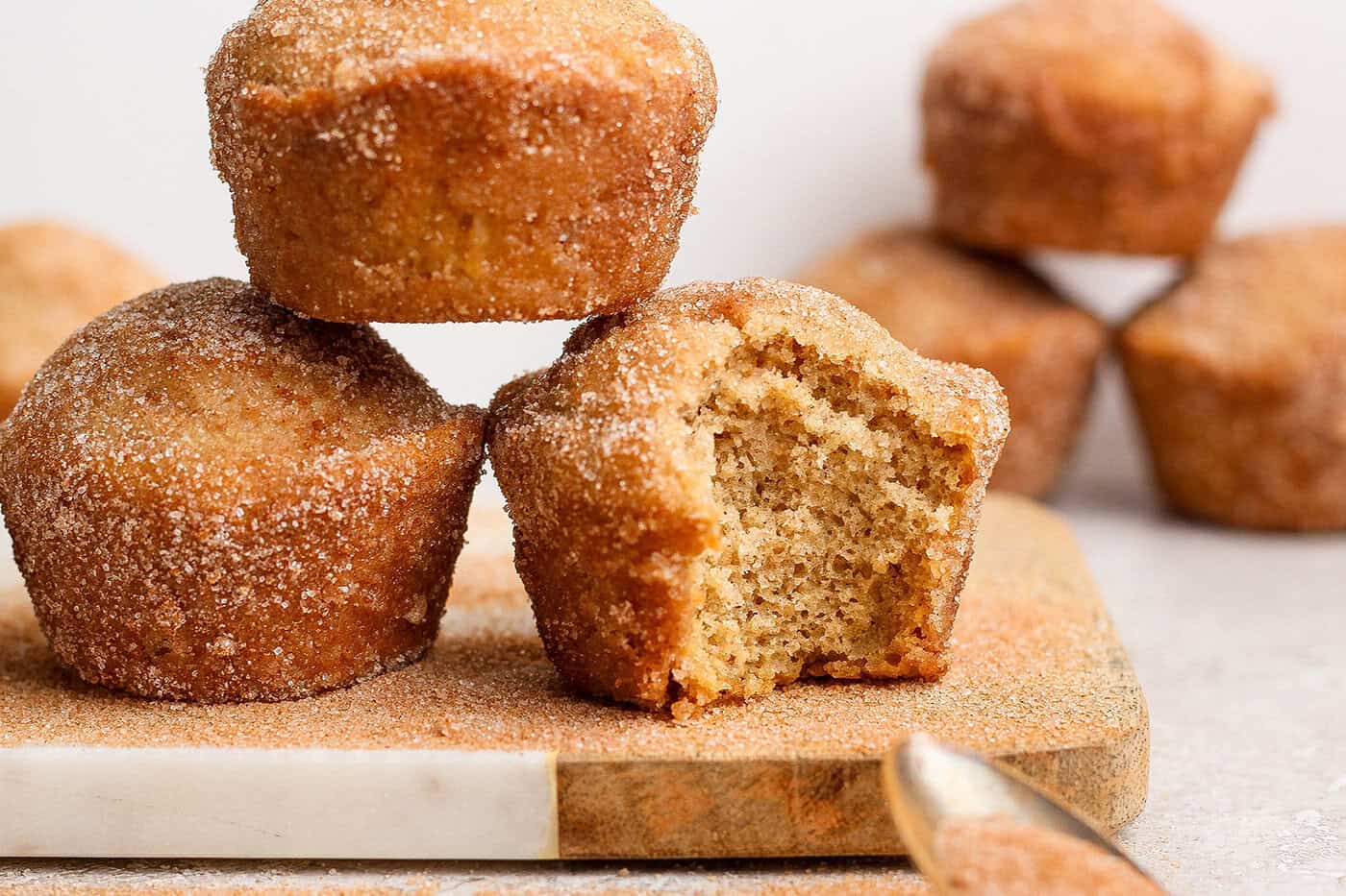 Cinnamon sugar doughnut muffins are easy to make and impossible to resist, with a moist, tender crumb and lots of cozy flavor. Perfection! Three cinnamon sugar doughnut muffins on wooden board, with one bitten into to show moist crumb