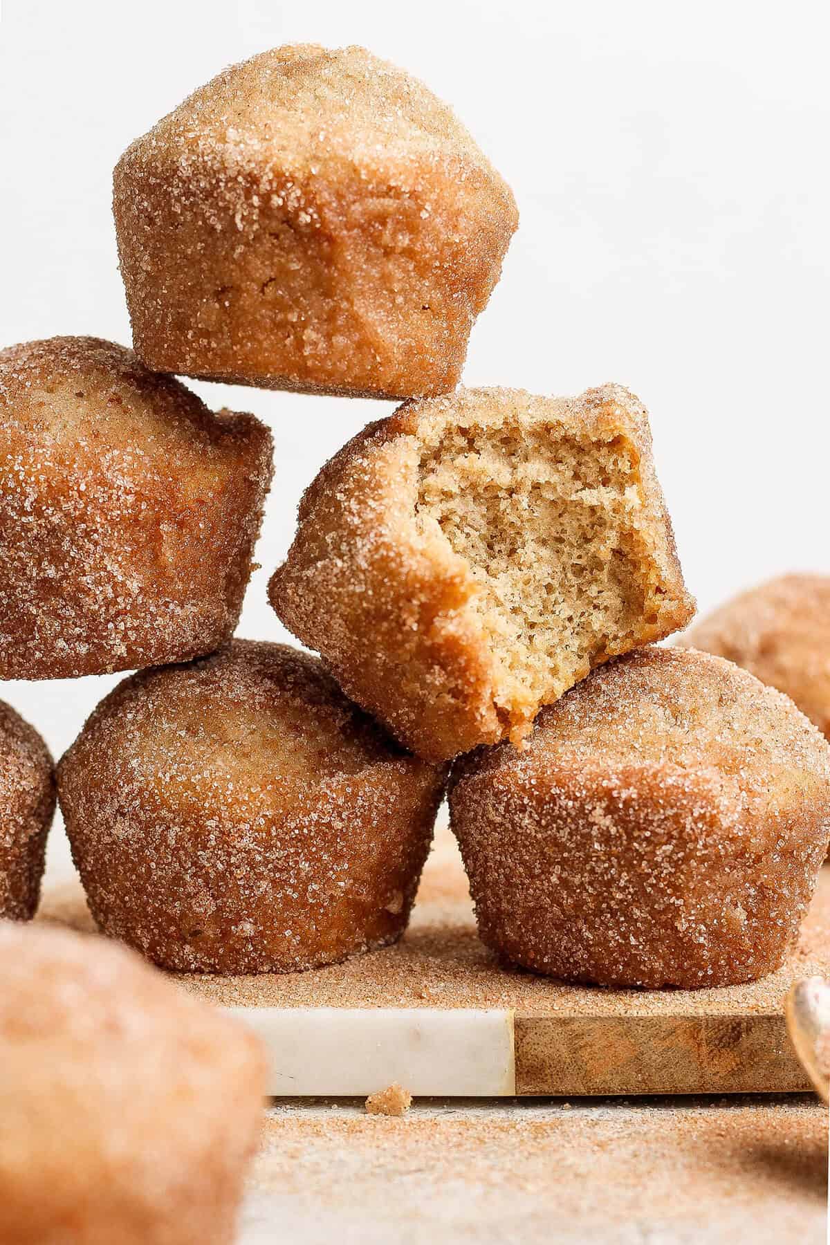 Cinnamon sugar doughnut muffins are easy to make and impossible to resist, with a moist, tender crumb and lots of cozy flavor. Perfection! Stack of cinnamon sugar doughnut muffins on wood board, with one muffin bitten into to show moist interior