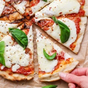 Hand pulling slice of grilled Margherita pizza from pie.