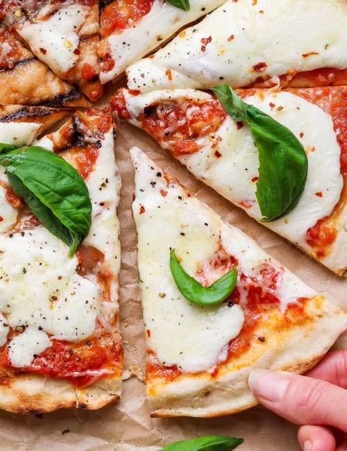 Hand pulling slice of grilled Margherita pizza from pie.