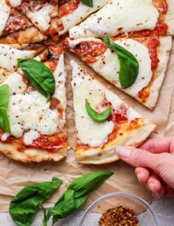 Hand pulling slice of grilled Margherita pizza from pie.